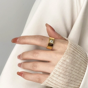 Gros plan d'une bague large dorée avec zircon portée sur le doigt, fond en tricot