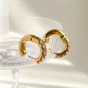 Gros plan de boucles d'oreilles créoles dorées avec cristaux blancs sur un verre