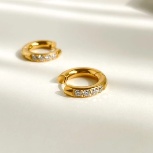 Gros plan de boucles d'oreilles huggie dorées avec cinq zircons blancs dans un style minimaliste