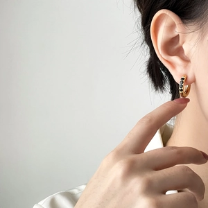 Gros plan d'une créole dorée ornée de pierres noires sur l'oreille du modèle
