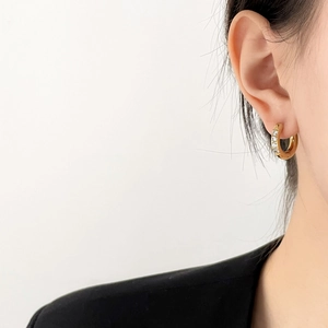 Gros plan d'une créole dorée avec cinq zircons blancs portée sur l'oreille du mannequin