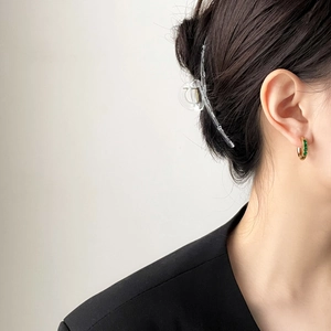 Détail de créoles dorées ornées de pierres vertes carrées portées par un mannequin chic