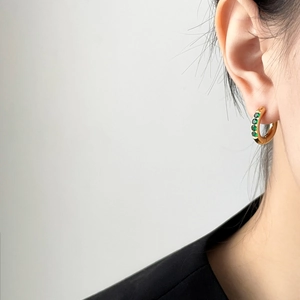 Élégante créole en or sertie de quatre pierres vertes portée sur l'oreille