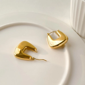 Elegant gold U-shaped geometric earrings set on a white ceramic plate for a luxury look