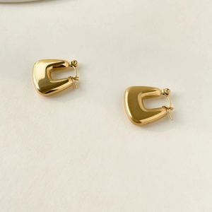 Macro shot of polished gold geometric U-shaped hoop earrings on a clean background