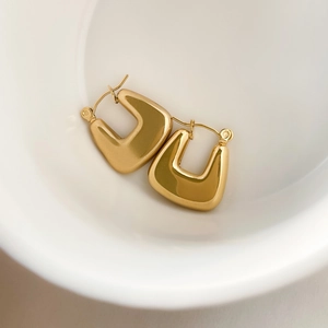 Detailed close-up of golden U-shaped geometric earrings on a white ceramic plate