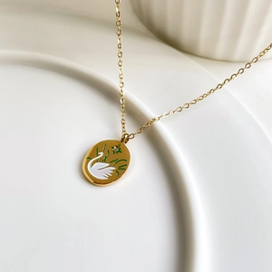 Detail of gold-plated titanium necklace with white swan enamel pendant and crystal inlay