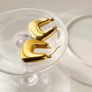 Close-up of polished gold U-shaped earrings hanging on a clear glass edge