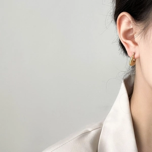 Detailed close-up of a polished gold U-shaped hoop earring worn on a model ear
