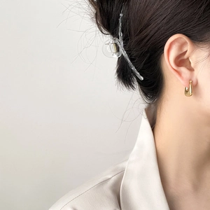Detail of elegant gold U-shaped earrings and transparent hair claw clip on a model