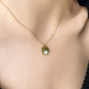 Detailed close-up of a gold-plated necklace featuring a swan enamel oval pendant on a model