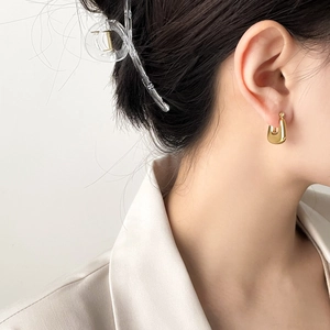 Close-up of elegant gold U-shaped hoop earrings worn by a model in a minimalist setting