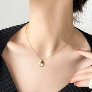 Close-up of gold plated titanium necklace with swan round pendant on black knitwear