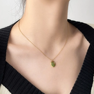 Detail of gold necklace with emerald green oval pendant and star-set zircon gemstone