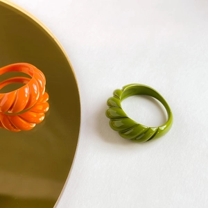 Detail of chunky croissant-style rings in vibrant orange and olive green enamel finish