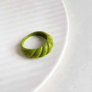 Close-up of grass green twisted texture ring with glossy enamel finish on ceramic plate