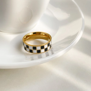 Detailed view of a gold checkered enamel ring on a white plate with soft shadows