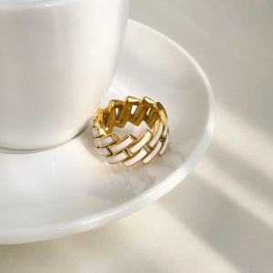 Detailed close-up of golden chain ring with white enamel inlay on a porcelain tray