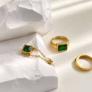 Close-up of emerald square zircon gold ring with textured band on white stone