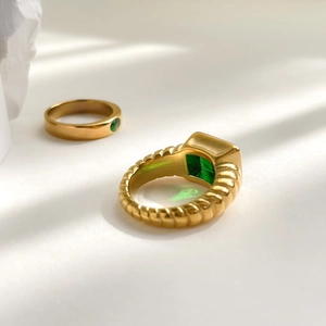 Macro shot of gold-plated rings with emerald green zircon stones and ribbed texture detail