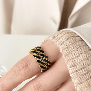 Close-up of a gold checkered ring with black enamel details worn on a finger