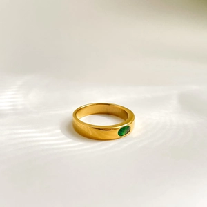 Macro detail of a gold minimalist ring featuring an oval-cut emerald green gemstone