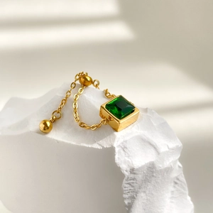 Close-up of emerald-cut green zircon ring with gold chain detail on white stone