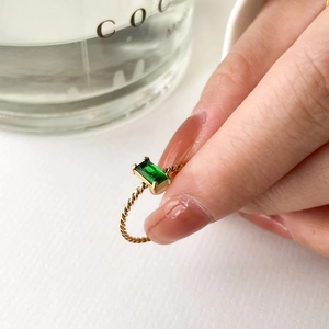 Vue rapprochée d'une bague torsadée dorée ornée d'un zircon vert émeraude au doigt