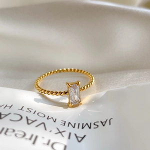 Gros plan d'une bague torsadée dorée avec un grand oxyde de zirconium taille émeraude