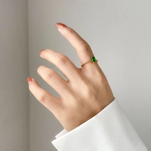 Détail d'une bague avec zircon vert coupe émeraude et anneau torsadé doré au doigt