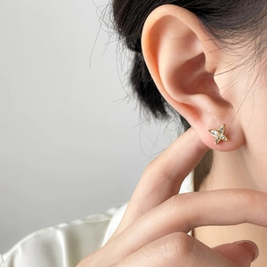 Close-up of small golden butterfly zircon earring worn on a model's earlobe