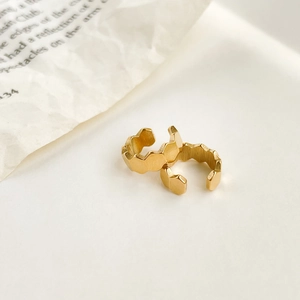 Close-up of golden geometric honeycomb cuff earrings on minimalist newspaper background