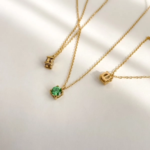 Detailed close-up of three gold necklaces with green zircon pendants in 4-claw setting