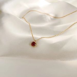 Close-up of gold 1-carat red zircon pendant necklace on white silk background