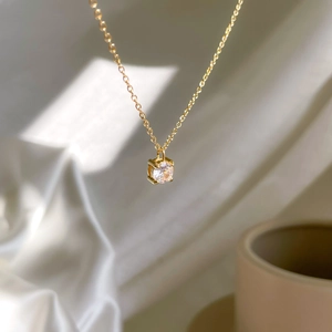 Detail of a gold-tone one-carat zircon pendant necklace with a round-cut stone on white silk