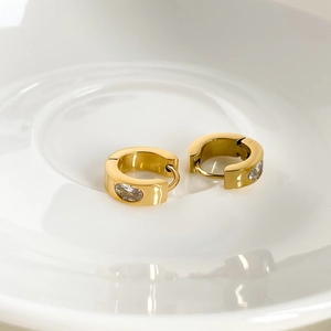 Detailaufnahme goldener Creolen mit ovalem Zirkonia auf weißem Keramiktablett