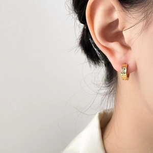 Nahaufnahme goldener Ohrring mit Zirkonia und polierter Oberfläche am Ohr des Models