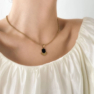 Détail de collier doré avec pendentif hexagonal noir et décor festonné sur le cou