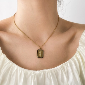 Détail du collier doré avec pendentif rectangulaire en émail noir et gravure soleil