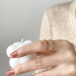 Detailed view of two gold-plated titanium rings set with orange and white zircons on hand