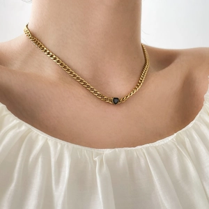 Gros plan d'un collier cubain doré avec pendentif cœur noir porté sur la clavicule