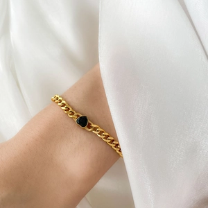 Bracelet à mailles cubaines dorées avec pendentif cœur noir porté sur tissu en soie