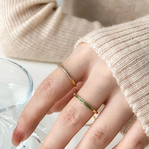 Detail of elegant gold-plated rings with white and emerald zircons worn by a model