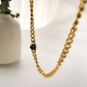 Détail macro du collier en chaîne dorée avec une pierre précieuse noire en forme de cœur