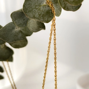 Détail d'un collier en or avec perles sur une feuille verte montrant l'éclat du métal