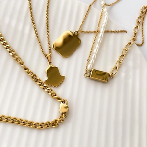 Détail de colliers dorés avec perles et pendentifs rectangulaires sur un plateau blanc