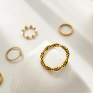Detailed close-up of a gold-plated twisted rope texture ring on a white ceramic stand