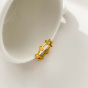 Detail of a gold geometric cross star ring hanging on a white ceramic cup edge