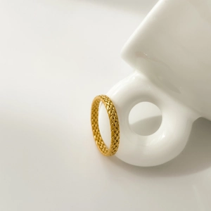 Detailed close-up of a gold woven texture ring resting on a white ceramic mug handle