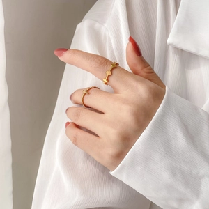 Set of two gold rings with wavy geometric design and beaded chain cross on a finger